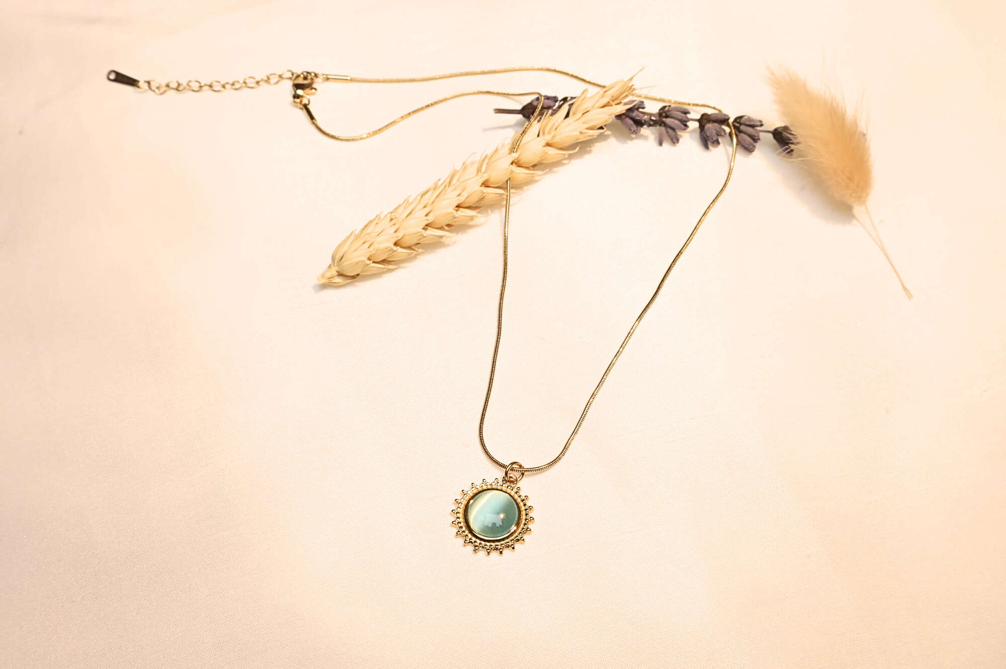 A gold-plated delicate chain featuring a radiant turquoise sun pendant, elegantly displayed with dried natural flowers.
